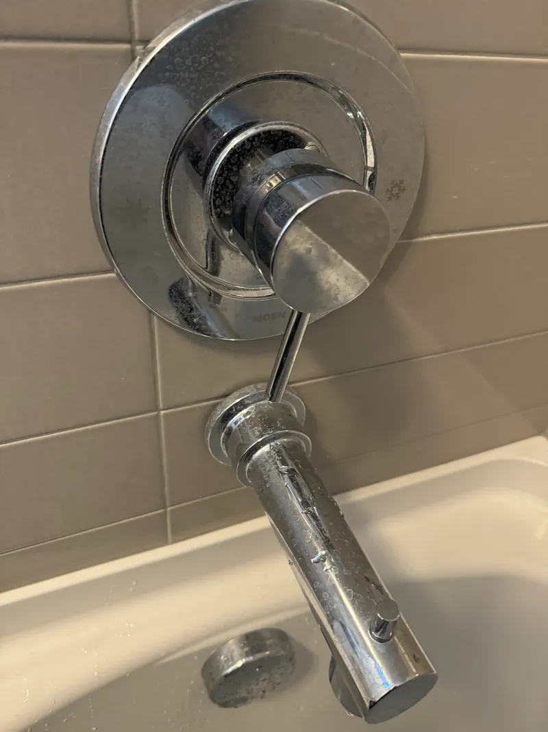 Chrome Moen shower valve and tub spout on gray tile wall